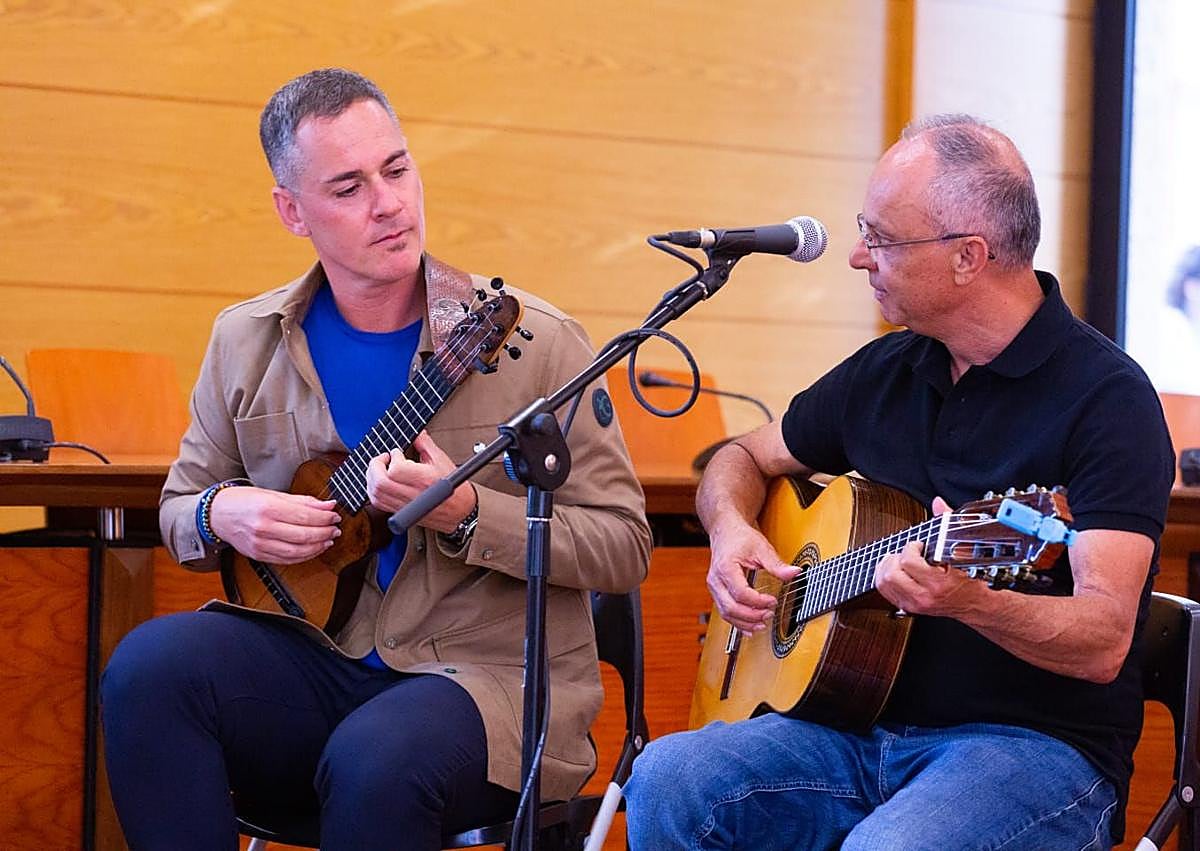 Imagen secundaria 1 - Arriba, Paqui Domínguez ayuda a Loly durante el acto. Debajo, los músicos Germán López y José Artiles. Y libro firmado por un beso de Loly hecho sello.