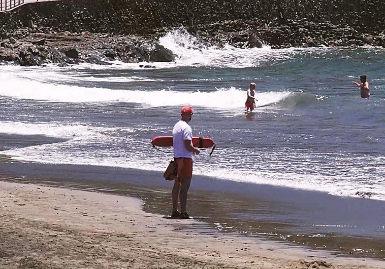 Un socorrista observa a dos bañistas en el agua, en una playa con oleaje y fuertes corrientes.