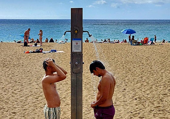 Dos jóvenes, en las duchas de la playa de Las Canteras este lunes.