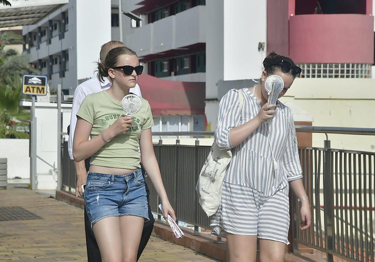 Dos mujeres combaten el calor con ventiladores de mano en el sur de Gran Canaria.