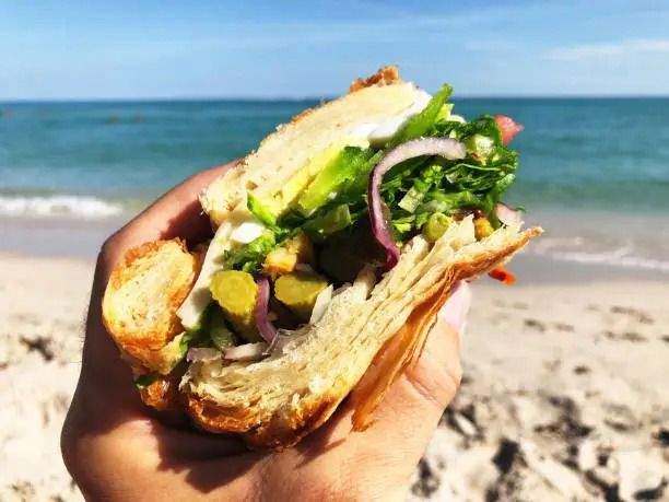 Mano sosteniendo un bocata en la playa.