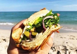 Mano sosteniendo un bocata en la playa.