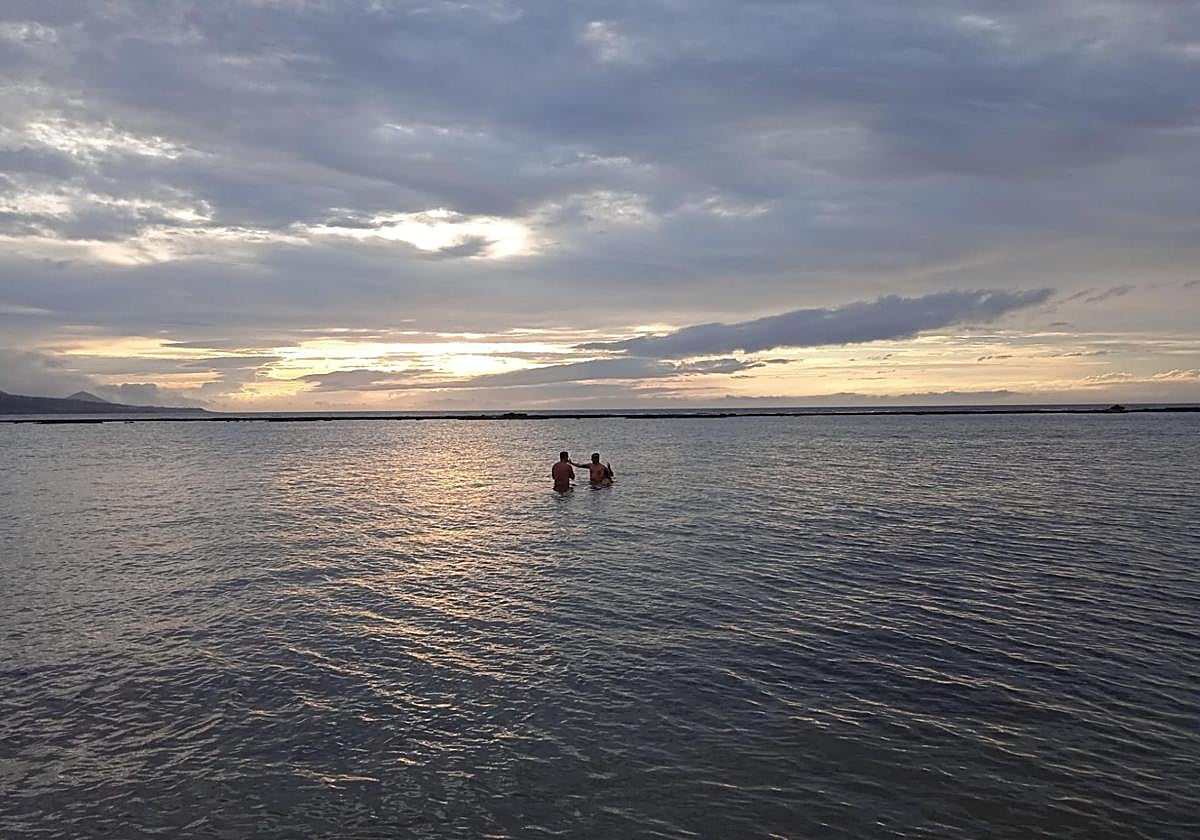 Imagen de dos bañistas en la playa de Las Canteras al atardecer.