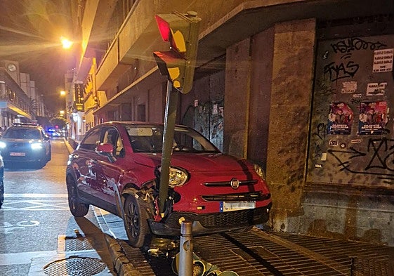 Imagen del coche empotrado entre la fachada del edificio y el semáforo.