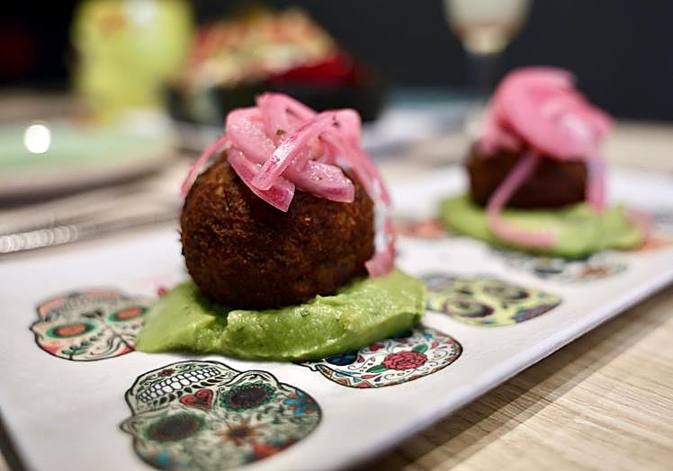 Cochinita pibil en formato buñuelo y acompañado de cebolla encurtida y guacamole.