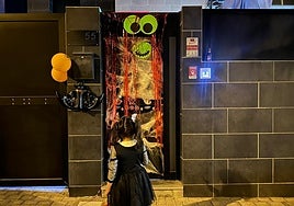 Imagen de una niña tocando en una casa decorada con temática Halloween.