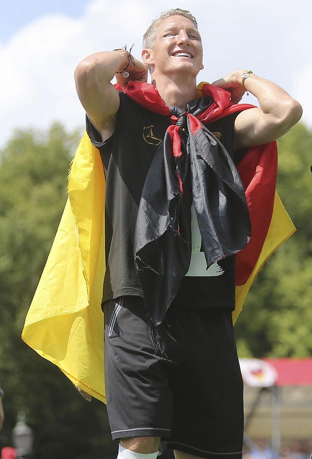 LA SELECCIÓN ALEMANA CELEBRA LA COPA DEL MUNDO CON MILES DE AFICIONADOS. Bastian Schweinsteiger se coloca la bandera nacional a modo de capa durante el multitudinario recibimiento de la selección de Joachim Löw en la Puerta de Brandeburgo en Berlín.