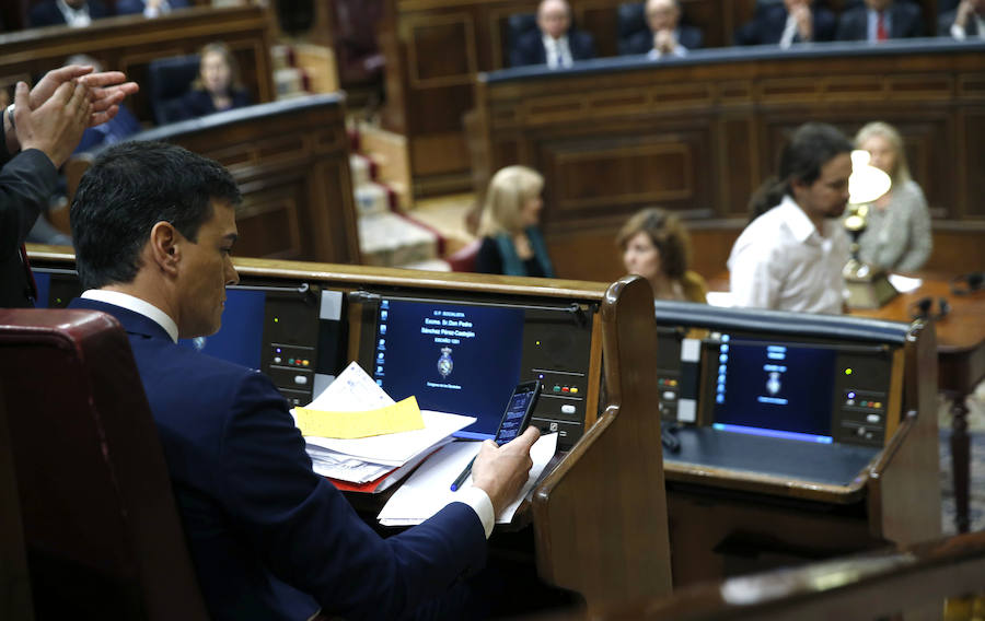 El secretario general del PSOE, Pedro Sánchez (i), observa su teléfono móvil mientras el líder de Podemos, Pablo Iglesias, se dirige a la tribuna del Congreso.