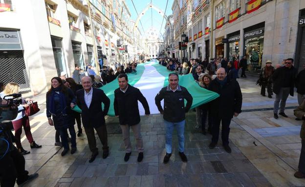 Juanma Moreno, junto a Francisco de la Torre y Elías Bendodo, sujetan la bandera andaluza en calle Larios.