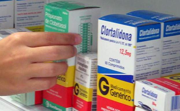 Foto de archivo de una persona cogiendo un medicamento de la estantería de una farmacia. 