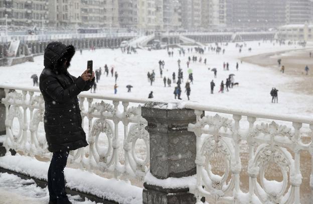 Una mujer toma una fotografía con su teléfono móvil en la playa de La Concha de San Sebastián, ayer, cubierta por la nieve. :: J. Herrero / efe