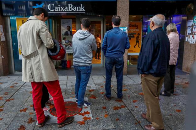 Varias personas hacen cola para entrar en una sucursal de CaixaBank en Barcelona. :: g. fuertes / reuters