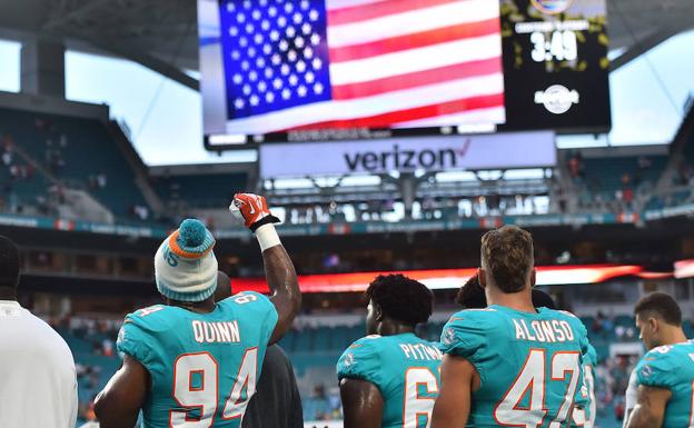 Jugadores de los Dolphins de Miami levantan el puño al sonar el himno en el estadio. 