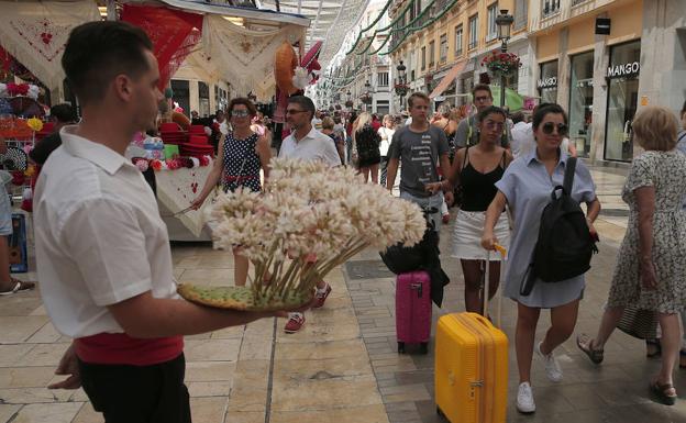 Imagen principal - Un biznaguero apura las últimas horas de feria en calle Larios, donde se cruza con feriantes y con turistas que dicen adiós. Aspecto de la plaza de la Constitución, ayer al mediodía, con un público que aunque menos numeroso no quiso dejar escapar las últimas horas de fiesta. Una joven vestida de corto sirve a la manera tradicional un vino dulce. 