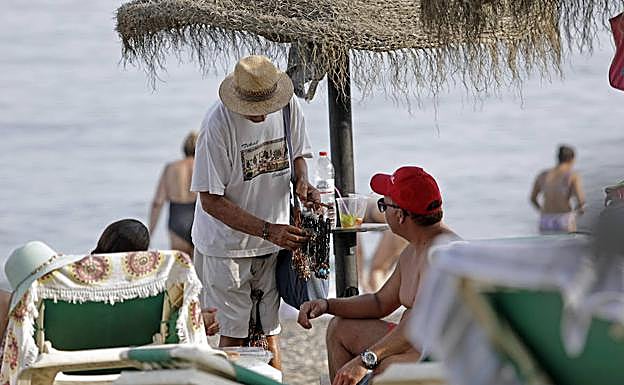 Imagen principal - Un turista se interesa por los colgantes. Un mantero vende sus productos en el paseo marítimo de Marbella. También venden comida y bebida en la playa.