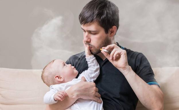 Un padre fuma mientras sujeta a su hijo.