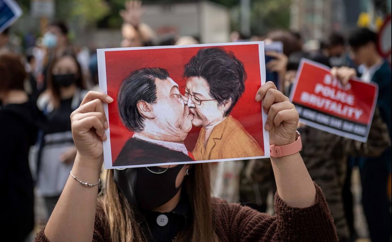 Una mujer sostiene un dibujo que representa al presidente de China, Xi Jinping (i) besando a la directora ejecutiva de Hong Kong, Carrie Lam (d).