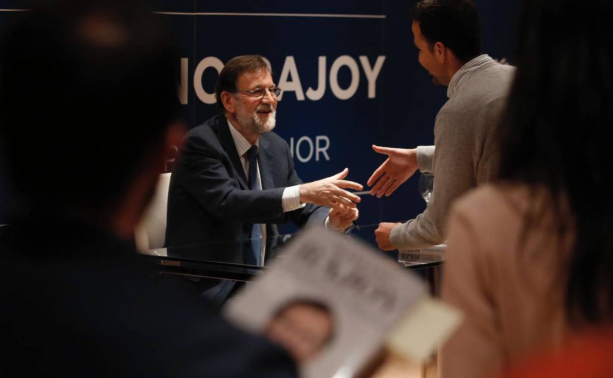 Rajoy da la mano a uno de los asistentes tras firmarle el libro.