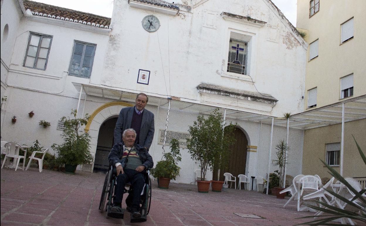 La imagen muestra a un dependiente en silla de ruedas y a su acompañante a las puertas del Asilo de los Ángeles. 