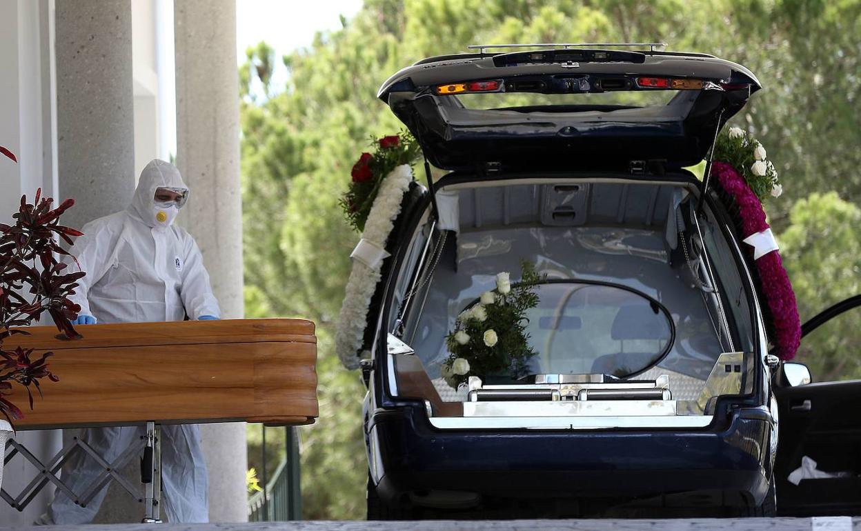 Dos operarios de Parcemasa, con sus equipos de protección, introducen un féretro en el coche fúnebre para enterrarlo. 