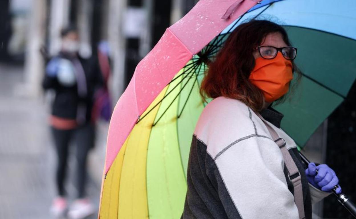 Una mujer con mascarilla se protege de la lluvia bajo un paraguas, ayer en la capital malagueña. 