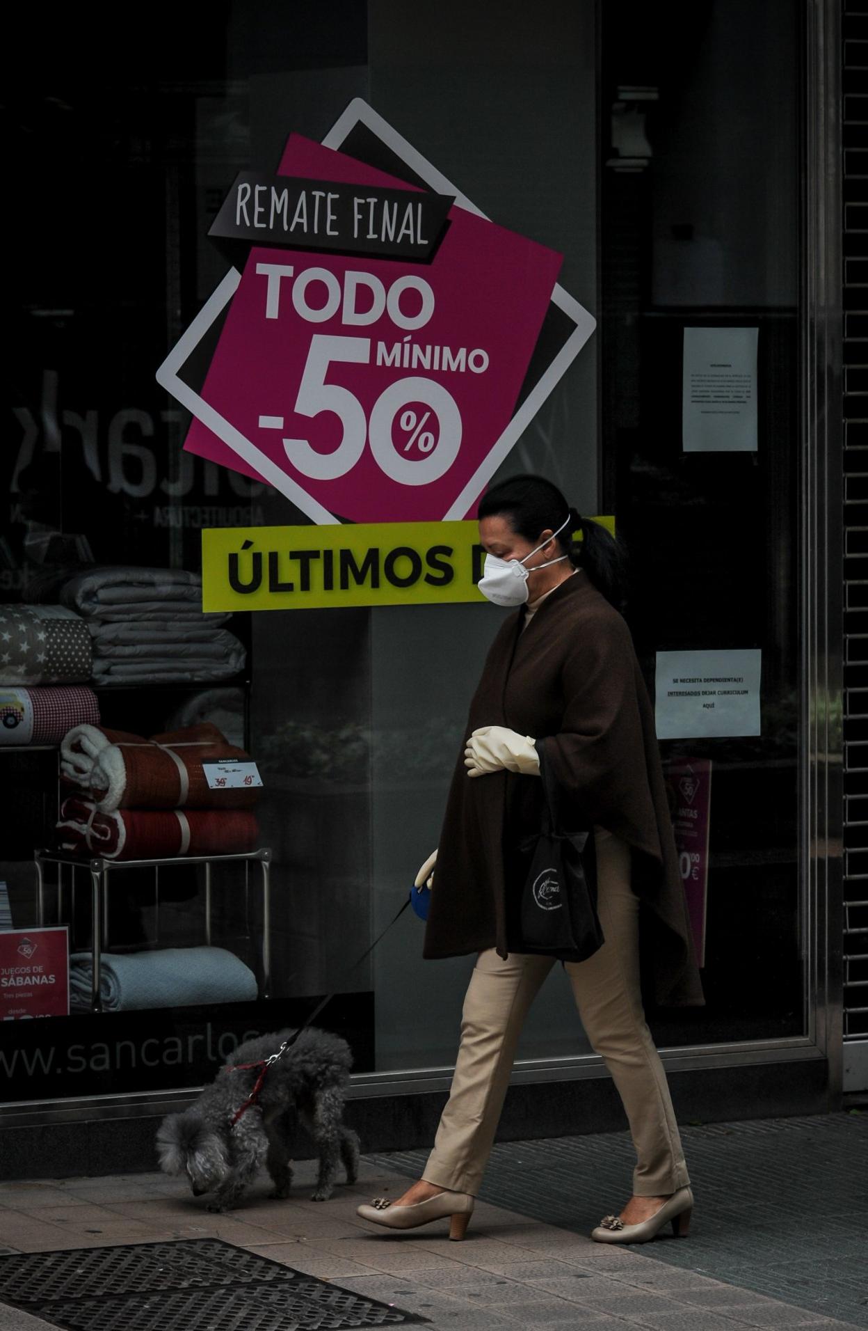 Una mujer pasa por delante del escaparate de una tienda de ropa con descuentos. igor aizpuru