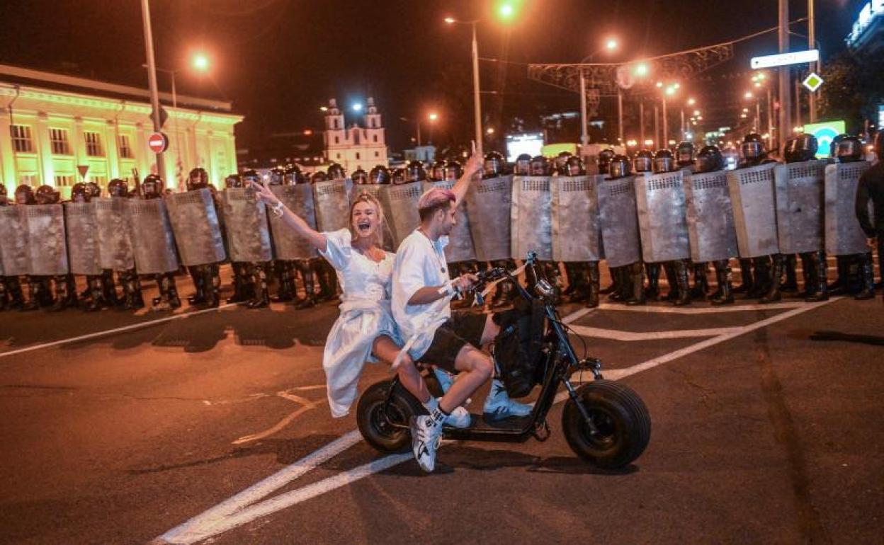 Manifestantes se pasean en motocicleta frente a un grupo de policías antidisturbios desplegados en una calle del centro de la capital bielorrusa.