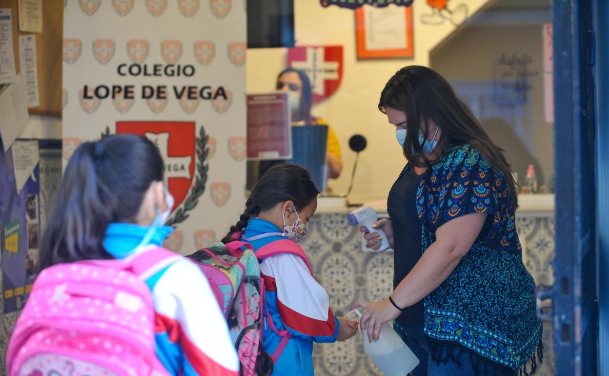 Unas niñas llegan al colegio, donde se les toma la temperatura y desinfectan las manos. 