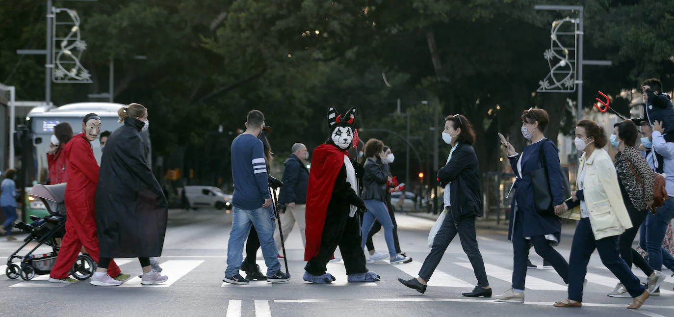 Personas disfrazadas se mezclan con las que llevan mascarillas en un paso de peatones en Málaga capital.