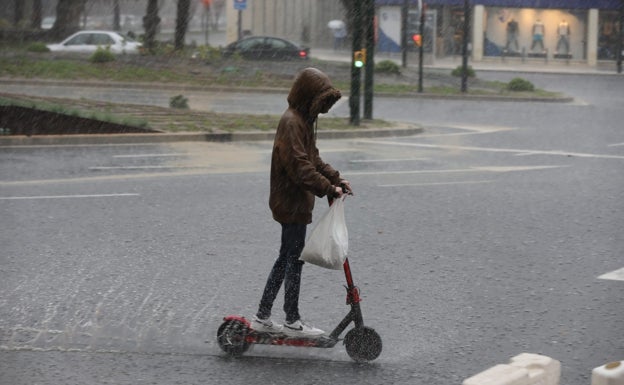 Un joven conduce un patinete bajo la lluvia, hoy en Málaga. 