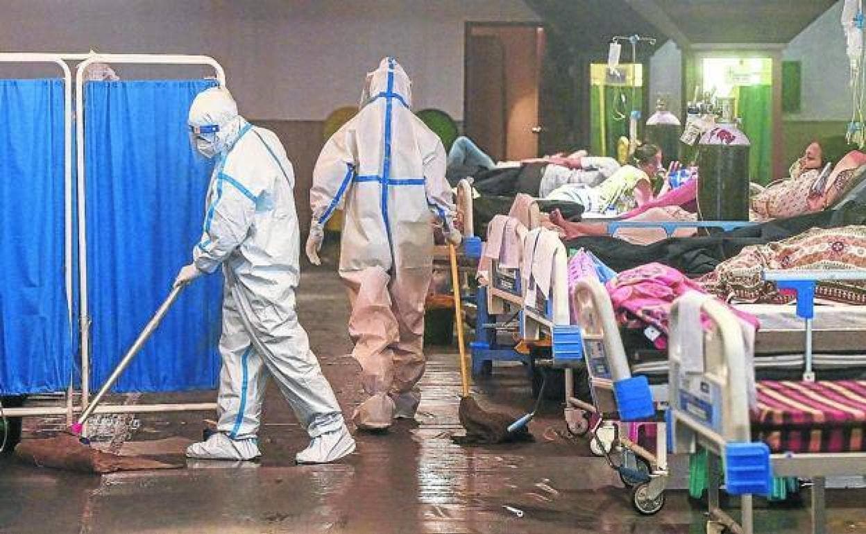 Dos trabajadores sanitarios limpian el suelo de una planta ocupada en precarias condiciones por pacientes de covid-19 en Nueva Delhi. 