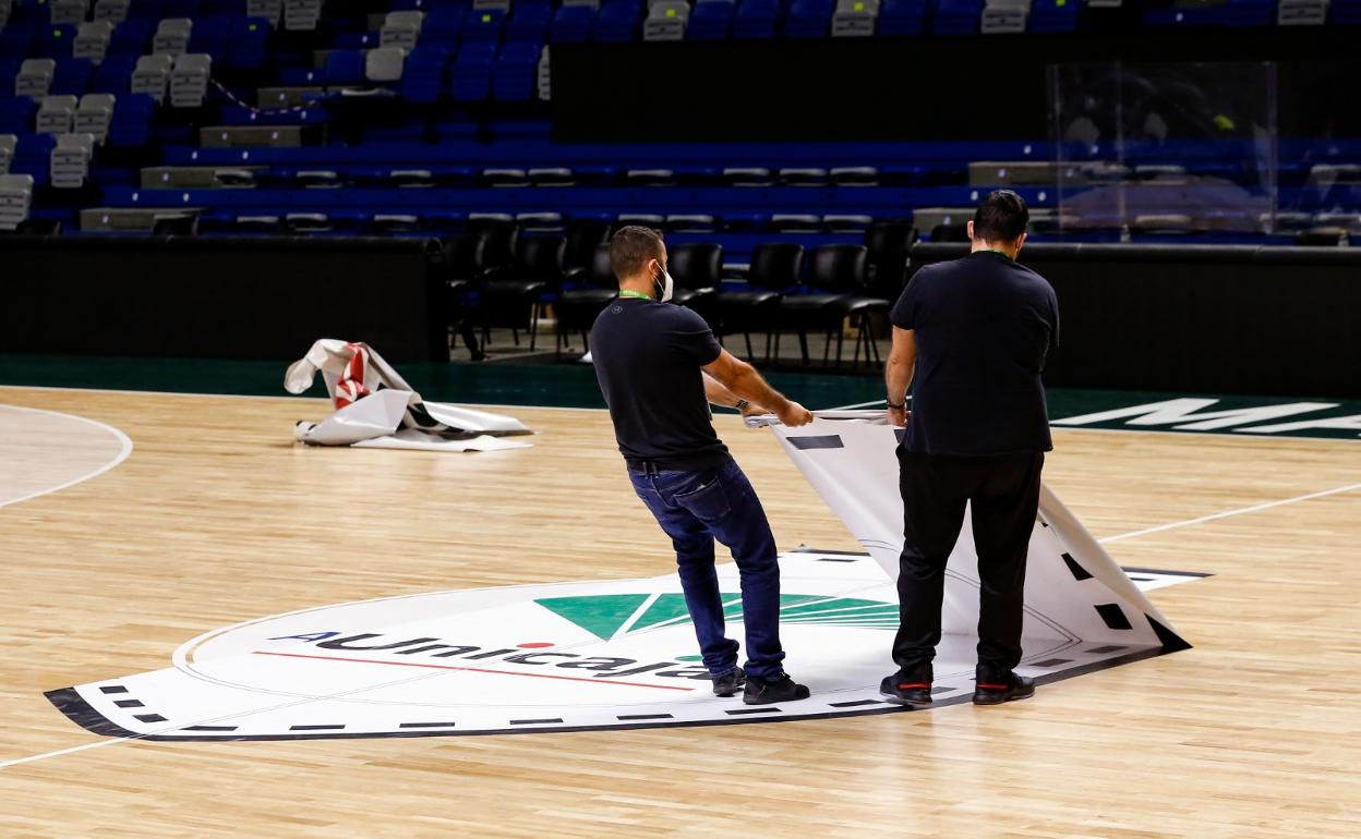 Dos operarios retiran el escudo del Unicaja del parqué del Palacio tras el último partido de la Liga. 