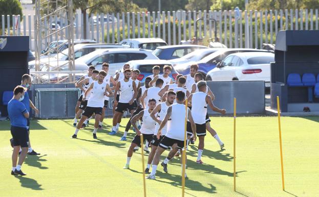 Jugadores del Málaga realizan ejercicios de calentamiento sobre el campo de la Federación. 