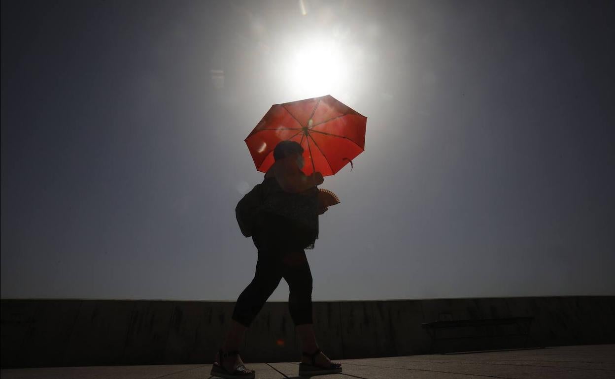 Una mujer camina resguardándose del sol con una sombrilla en Córdoba. 