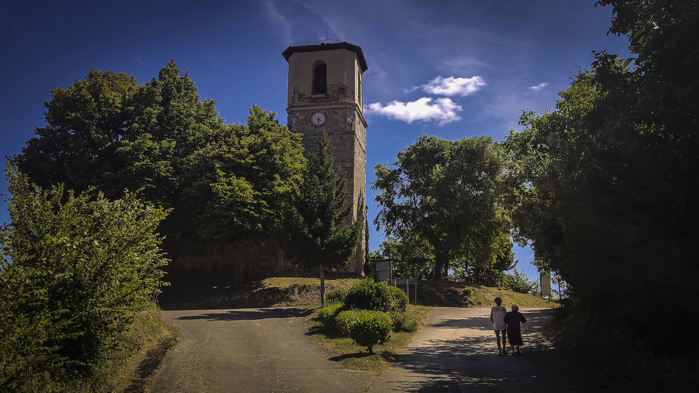 En Villambistia, ya en Burgos, es fácil reconocer los estragos de la España vaciada. En la imagen, una mujer ayuda a una anciana a dar un paseo junto a la iglesia parroquial de San Esteban.