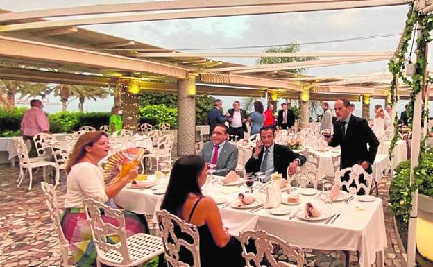Imagen principal - La cena se celebró en la pérgola del Real Club Mediterráneo, junto a la Farola de Málaga. Abajo, José María Amaya repartía biznagas al entrar en el evento y detalle de los trofeos 