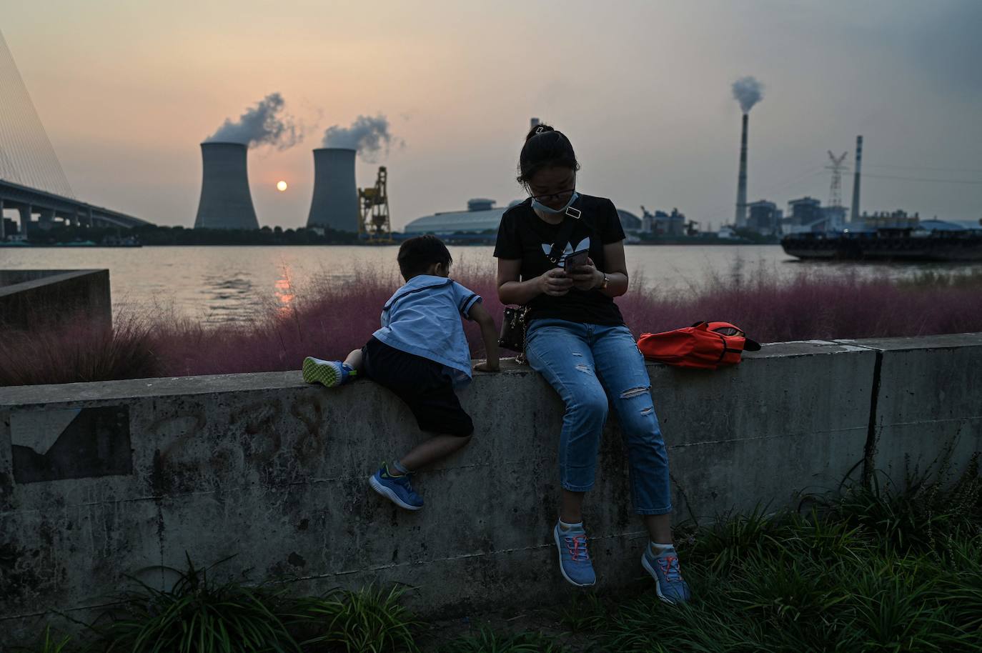 Una mujer y un niño se sientan en la ribera del río Huangpu, al otro lado de la central eléctrica de carbón y electricidad de Wujing en Shanghai.