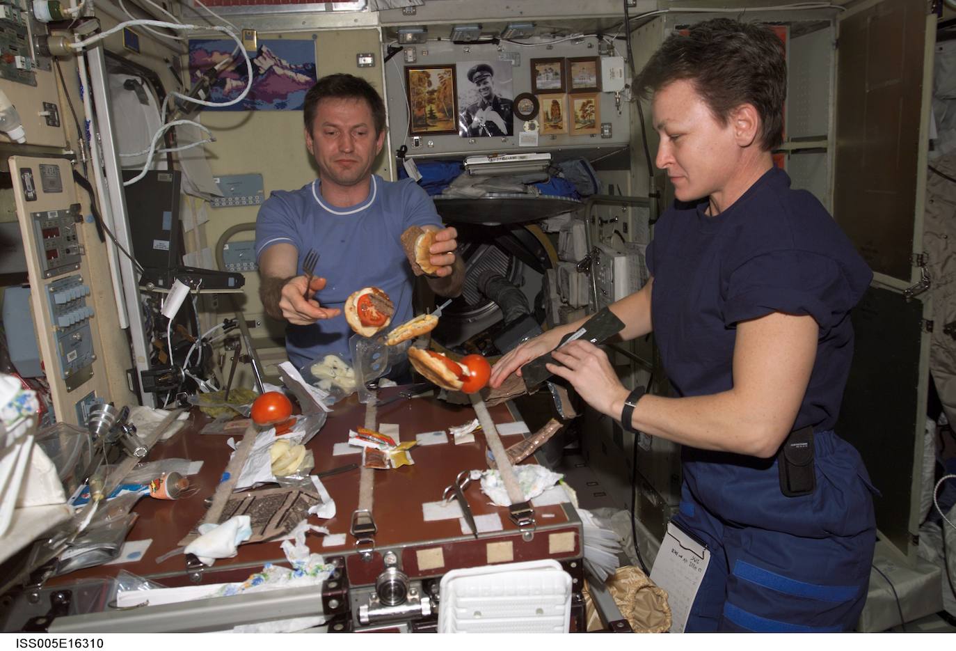 los ingenieros de vuelo Sergei Treschev y Peggy Whitson comen hamburguesas en la zona de la cocina en el Módulo de Servicio Zvezda, durante la Expedición Cinco en la Estación Espacial Internacional.