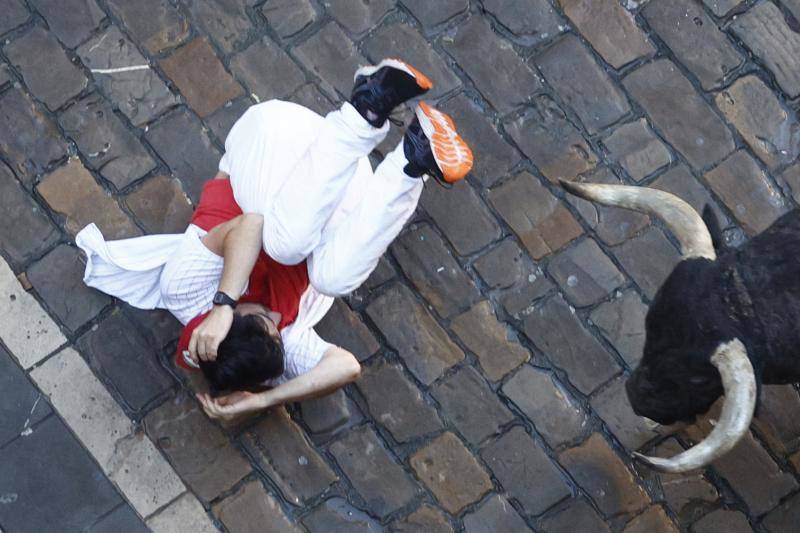 Un mozo caído ante uno de los toros de la ganadería de José Escolar durante el tercer encierro de San Fermín.