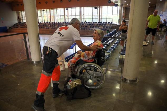 Un sanitario de Cruz Roja atiende a una vecina desalojada por el incendio de Alhaurín el Grande, en Málaga