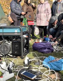 Imagen secundaria 2 - Reparto de ayuda humanitaria a residentes de la ciudad de Jersón mientras otros cargan sus móviles en generadores. 