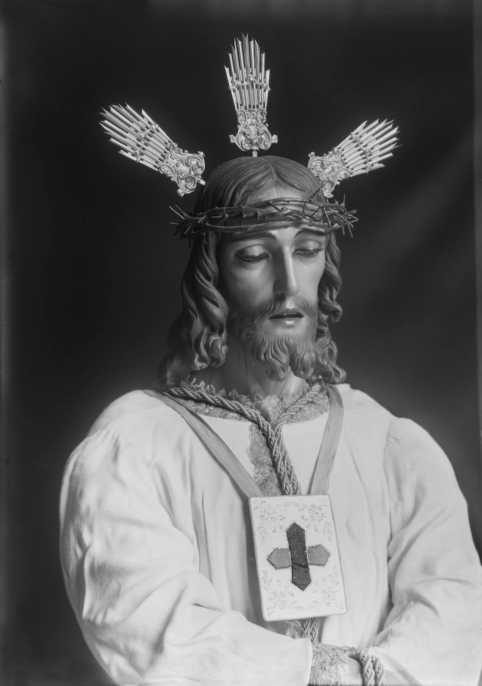 La talla de Jesús Cautivo es una obra del escultor granadino José Gabriel Martín Simón, realizada en 1938. Su llegada a Málaga vino cargada de polémica, dado que Luis Cambronero, académico de San Telmo, no estaba de acuerdo con el desnudo de la imagen, acorde con el pasaje de la Presentación al Pueblo. A raíz de esta queja, el Obispado prohibió su bendición a menos que se cubriera el cuerpo con una túnica. Es por ello que el Señor de Málaga luce esta prenda desde el mismo momento en que fue consagrado, el 19 de marzo de 1939. Eso sí, la peculiaridad radica en que aquella túnica, al igual que ahora, era de color blanco, un anacronismo iconográfico aceptado por el pueblo y la Iglesia, por cuanto, en realidad, esta tonalidad no se corresponde con el momento plástico representado. En la instantánea se aprecia las primeras potencias de metal del Señor, ejecutadas hacia 1945.