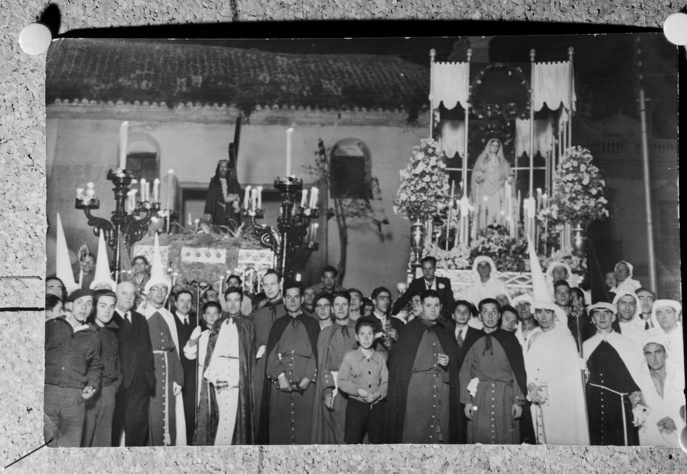 Fotografía de los integrantes del cortejo de la Cofradía del Rocío, con la cara descubierta, ante los titulares. El momento corresponde al Martes Santo de 1941, año en que se estrenaron el trono del Nazareno de los Pasos, obra de José Rueda, y el palio de la Virgen del Rocío, confeccionado con damasco de seda. Como se observa, en el lateral de la iglesia de San Lázaro existía una puerta que permitía la salida de los tronos desde su interior. Esta puerta, hoy cegada, se abrió en 1928.