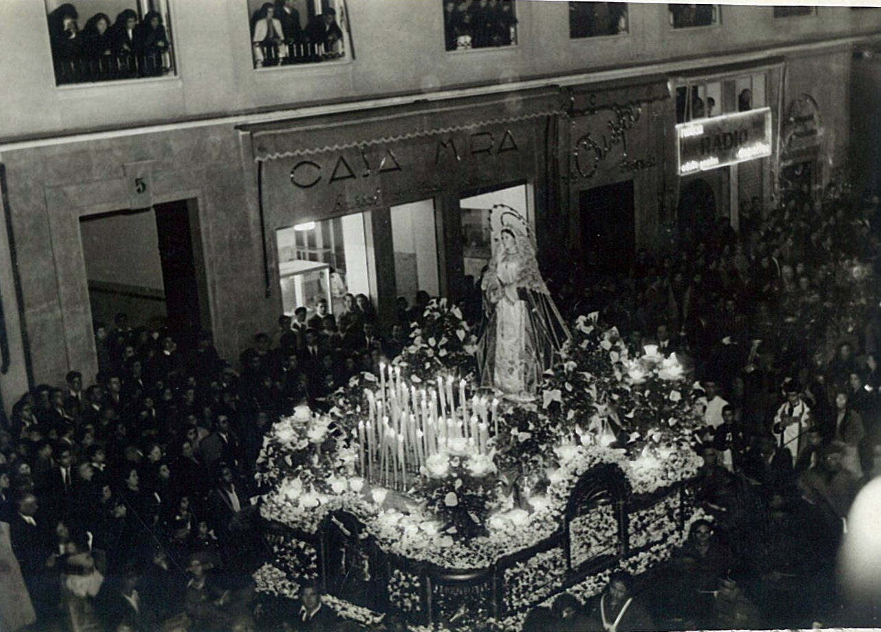 La Virgen del Rosario en sus Misterios Dolorosos salió por primera vez en la Semana Santa de 1940. Dos años más tarde estrenó un trono de Bernardo Pérez Rivero al que, al año siguiente, se le acopló un palio. En la instantánea puede observarse el paso del trono por la calle Larios.