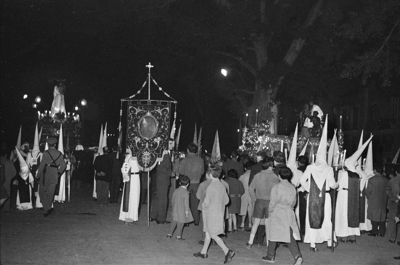 Este momento del Martes Santo de 1959, minutos antes de las once de la noche, se produjo el encuentro entre el Señor de la Humillación, que caminaba por el centro de la Alameda, y el grupo escultórico de la Sentencia, que acababa de acceder por el lateral y era la cofradía que cerraba la jornada por el recorrido oficial. En primer término, el estandarte con la pintura de la imagen cristífera de la corporación perchelera. Los bordados son de la Casa Gavín, de Valencia, ejecutados en 1923.