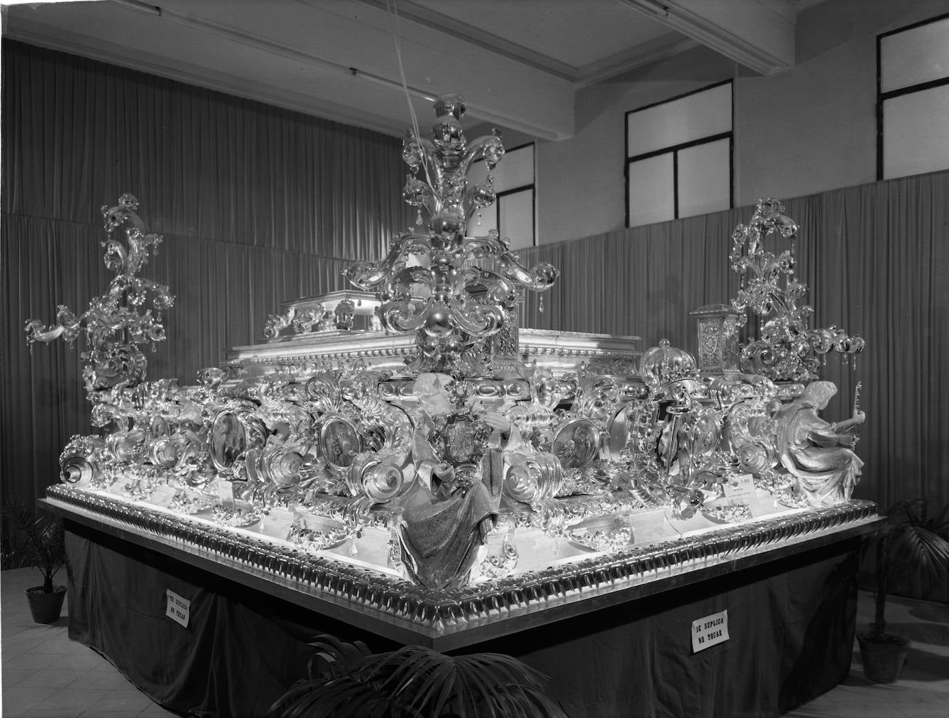 Nicolás Prados López realizó un nuevo trono para la Virgen del Amor en el año 1963 que fue presentado en la exposición de estrenos de la Semana Santa de ese año realizada en la Casa de la Cultura, a la que corresponde esta fotografía. Este año también reformó y amplió el trono del Cristo.