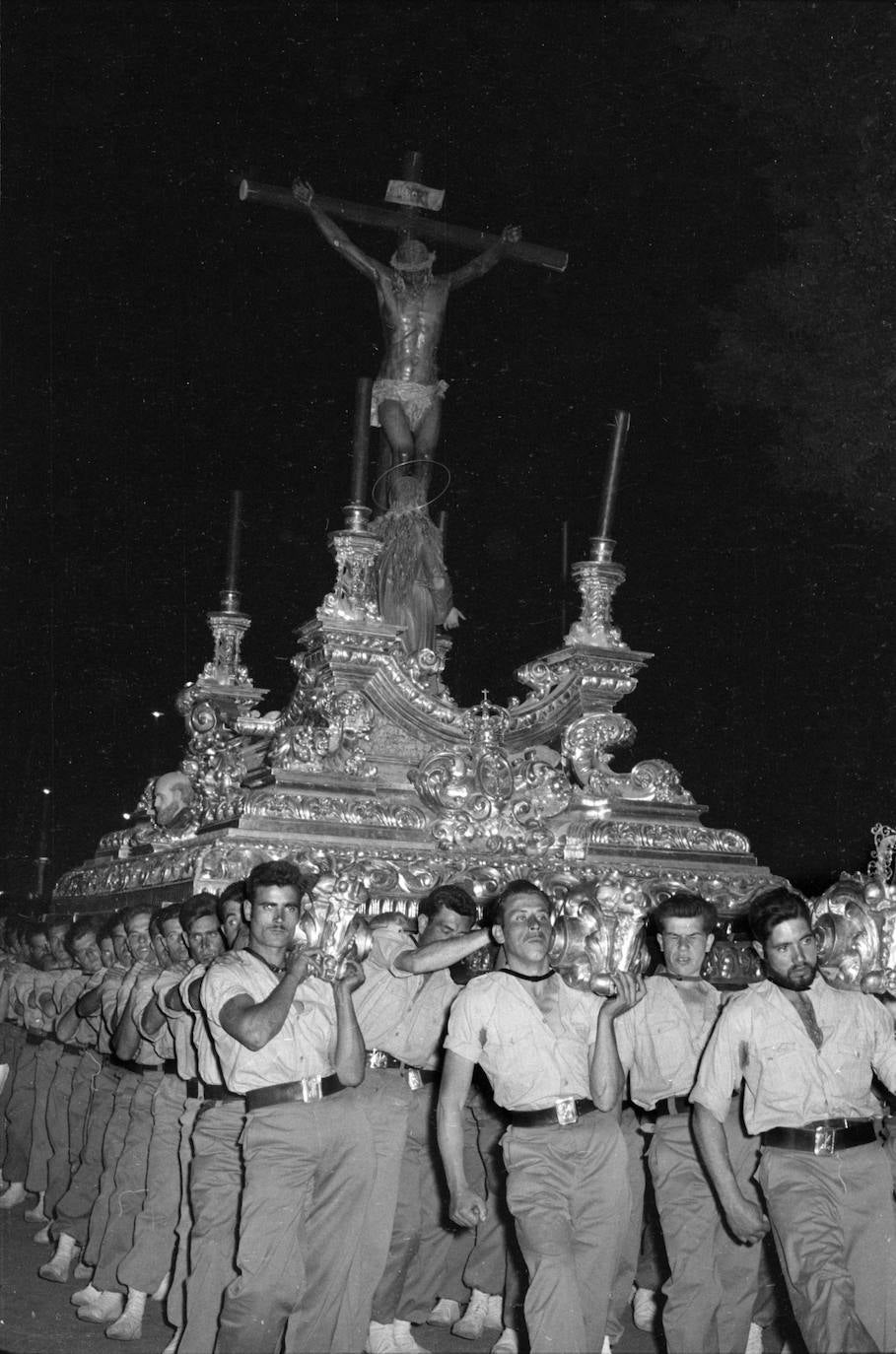 El trono del Cristo de la Buena Muerte, obras ambas –imagen y andas procesionales– de Francisco Palma Burgos, es portado por caballeros legionarios. La cofradía recorre la Alameda Principal y el objetivo de Arenas capta las expresiones de esfuerzo de tan singulares hombres de trono, que llevan el chapiri legionario asido al cuello.