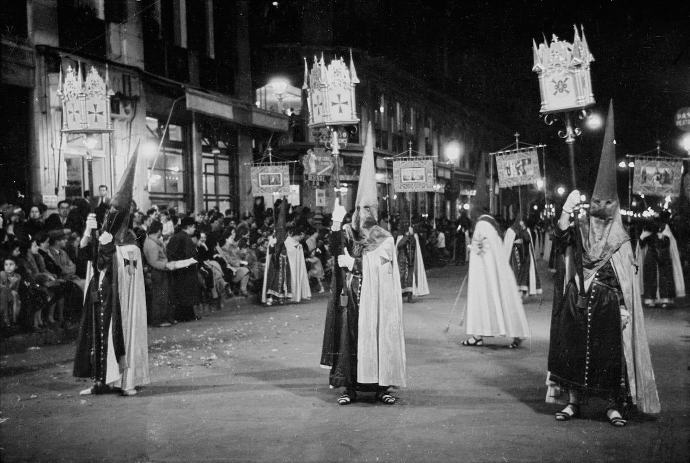 Viernes Santo de 1946. Obsérvese el cuerpo de insignias de entonces, encabezado por tres nazarenos vestidos con túnica y capirote azul, capa blanca, calcetines blancos y sandalias, portando unos singulares faroles de planta cuadrada con cruces en cada una de sus caras.