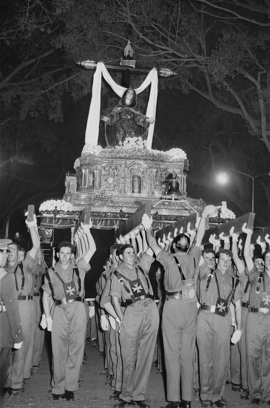 La vinculación de la Cofradía del Santo Traslado y la Soledad de San Pablo con los regimientos Aragón 17 y Melilla 52 fue una nota característica de la hermandad trinitaria. En esta fotografía tomada en la Semana Santa de 1960, se ve a los militares portando el trono de la Soledad de San Pablo por la Alameda Principal. Los soldados levantan a pulso a la Virgen y reciben las indicaciones de un suboficial. Los militares fueron sustituidos en el trono, años más tarde, por jóvenes que se incorporaron a la popular hermandad trinitaria para llevar ambos tronos.