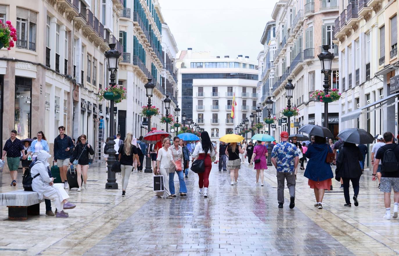 Turistas y malagueños con paraguas en la calle Larios